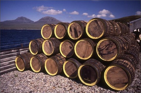 Casks at Bunnahabhain Distillery, Islay, with the Sound of Islay and the Paps of Jura behind: every one of these loses a little more each year it sits here.