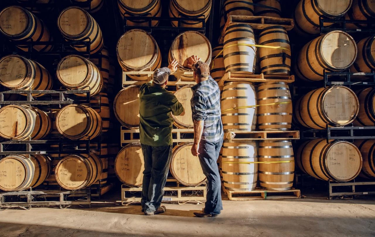 Two men examining a wooden cask in a warehouse